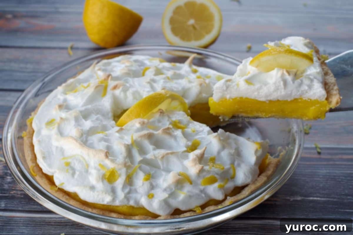 a piece of lemon pie being lifted out of a whole pie, with a lemon cut in half in background