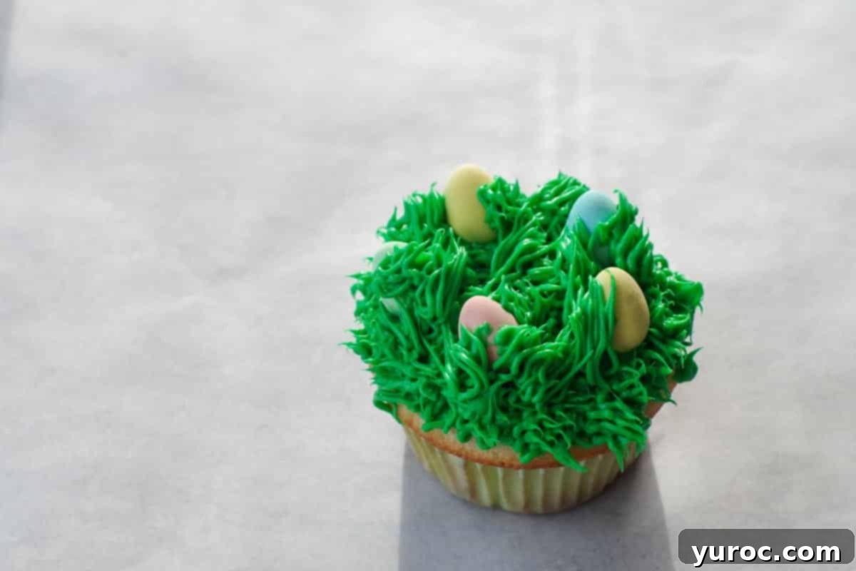 Mini Egg Hunt Cupcake Treasures 13 A cupcake with mini eggs, where additional green frosting is piped subtly around the eggs to integrate them into the 'grass' design.