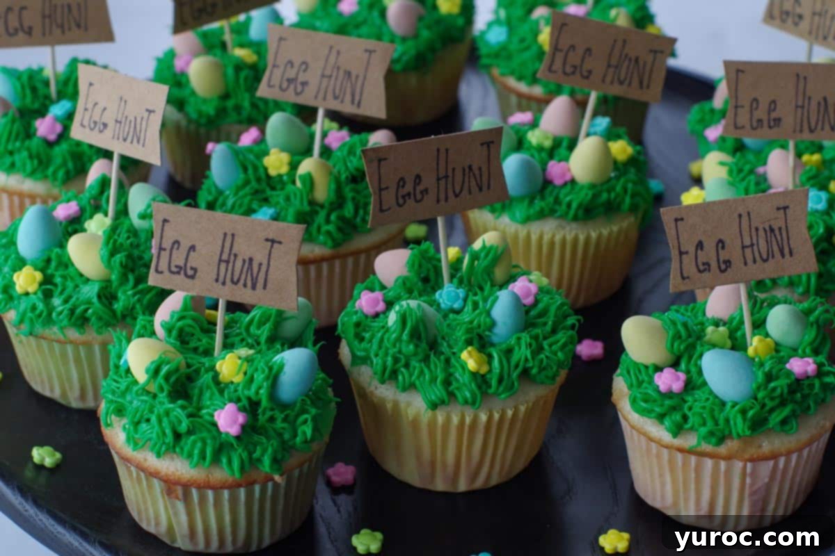 Mini Egg Hunt Cupcake Treasures 15 A dozen exquisitely decorated Easter cupcakes, each featuring mini eggs nestled in green grass frosting, elegantly displayed on a black platter.