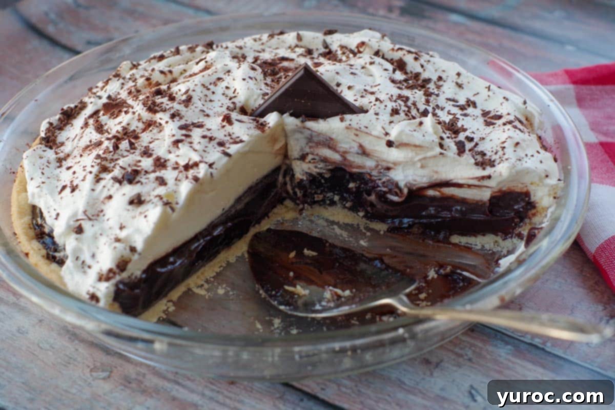 Timeless Chocolate Pie 11 Old fashioned chocolate pie in a glass pie pan, with two slices removed and a pie lifter in the empty space, against a red checkered tea towel