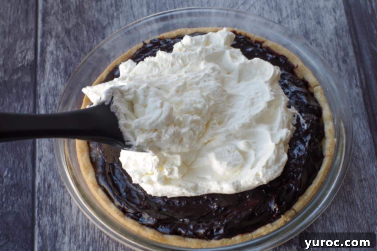 Timeless Chocolate Pie 7 Whipped cream being spread generously onto the top of a chocolate pie