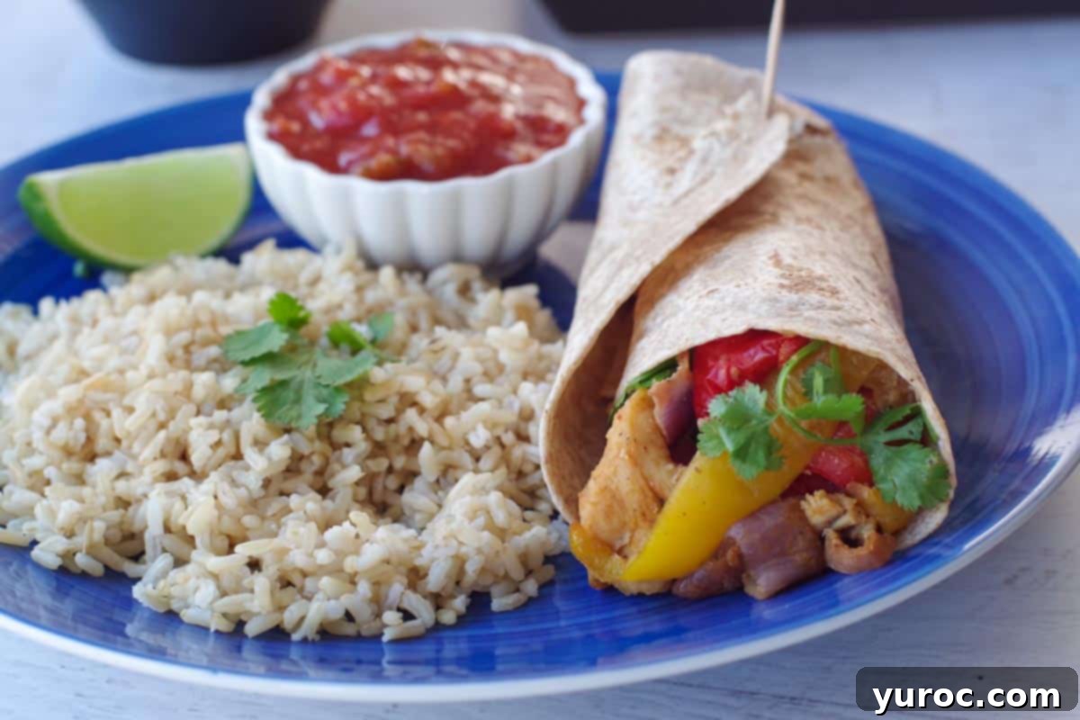air fryer fajitas in a wrap, on a blue plate with rice, salsa and a wedge of lime