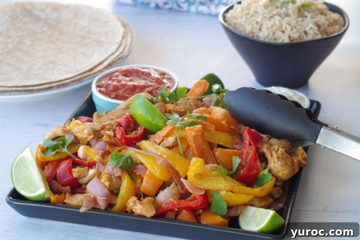 Cooked fajita filling on a black platter with salsa and lime wedges, as well as rice and tortillas in the background