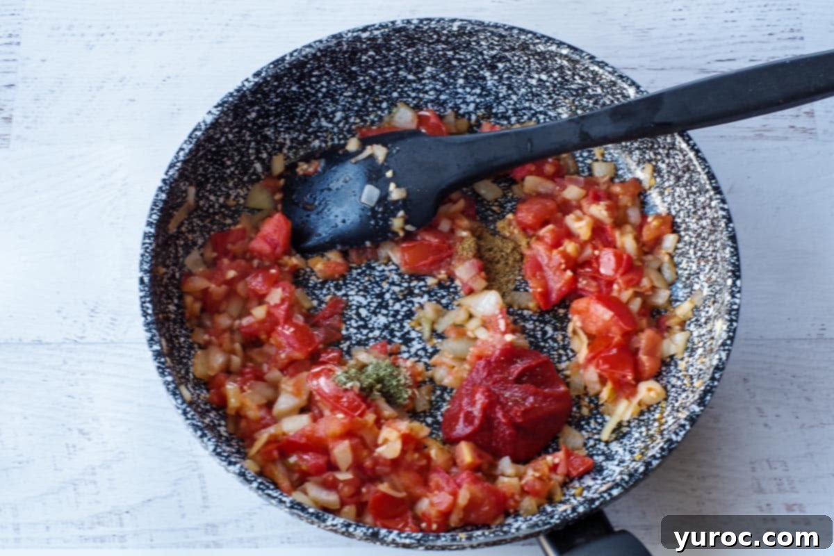 tomato paste and spices added to the skillet, with black spatula