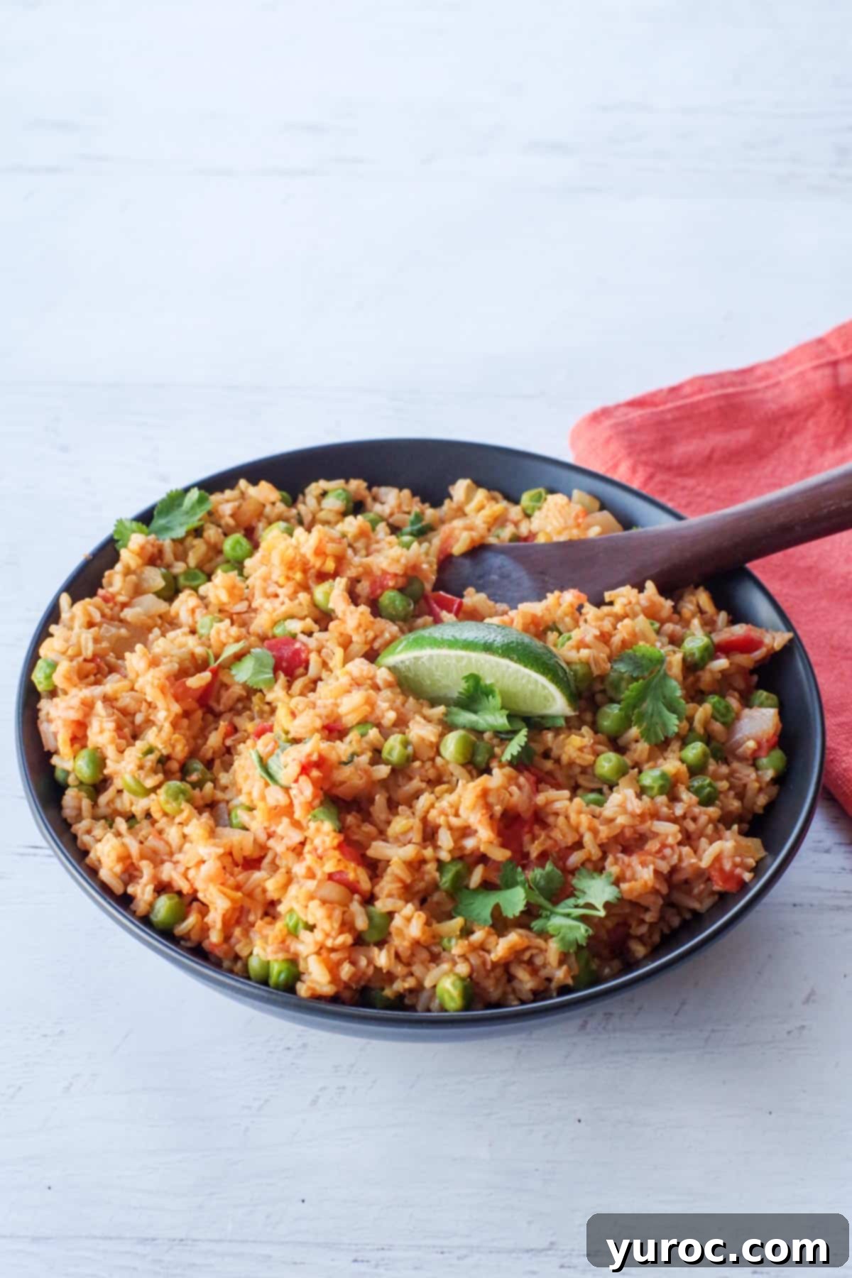 Spanish brown rice in a black bowl with a wooden spoon and an orange napkin on the side