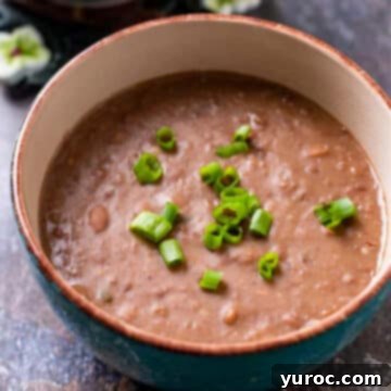 What to Serve with Carnitas: 25 Irresistible Recipes 9 Slow cooker refried beans in a brown bowl, garnished with green onions.