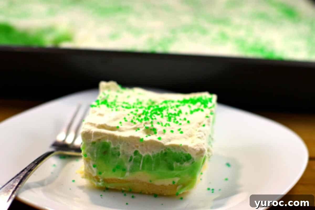 Pistachio Pudding dessert on a white plate with a pan of more pistachio dessert in the background.