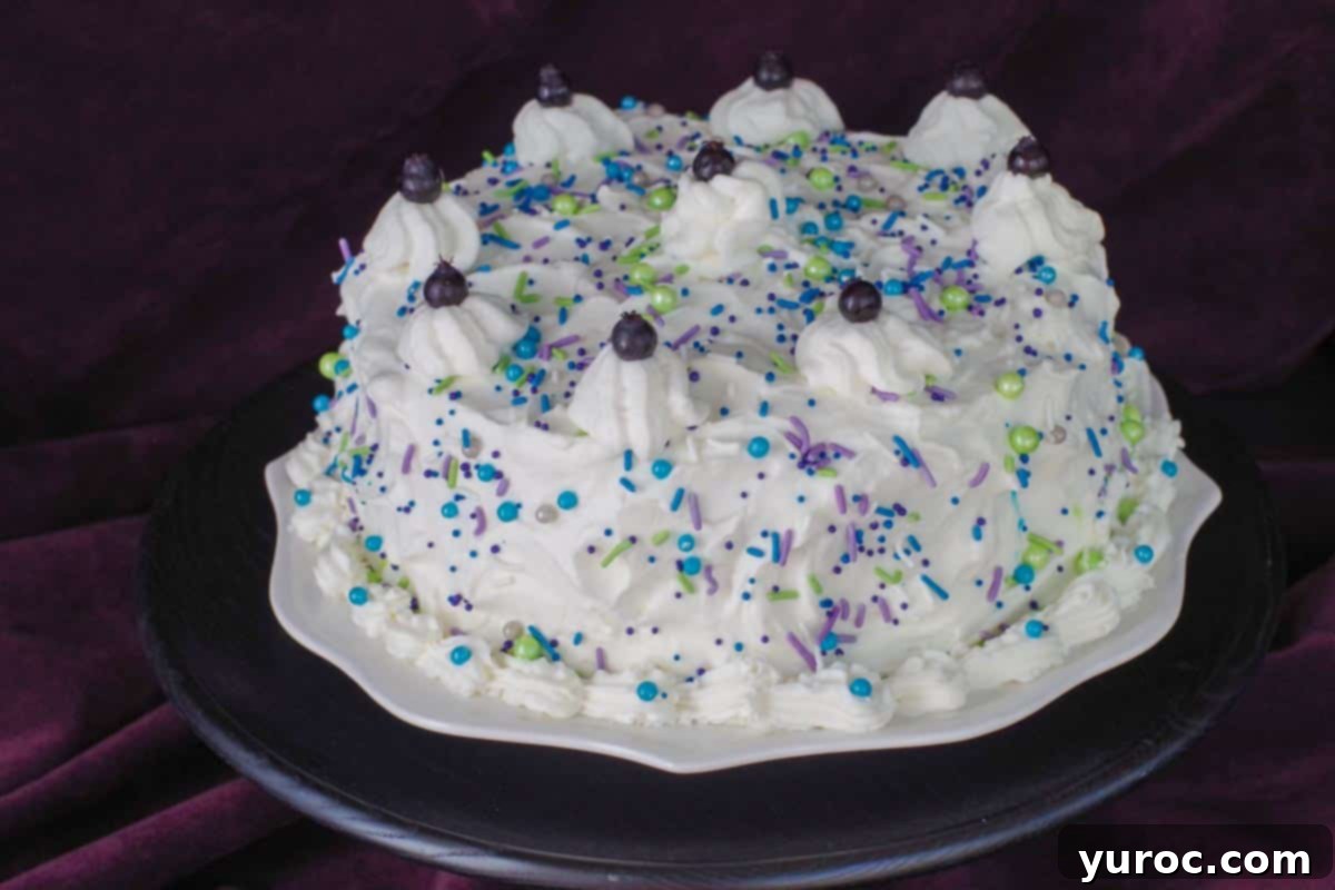 A beautifully decorated whole Saskatoon berry cake with delicate white sprinkles scattered on top, presented on a white plate which rests on an elegant black platter.