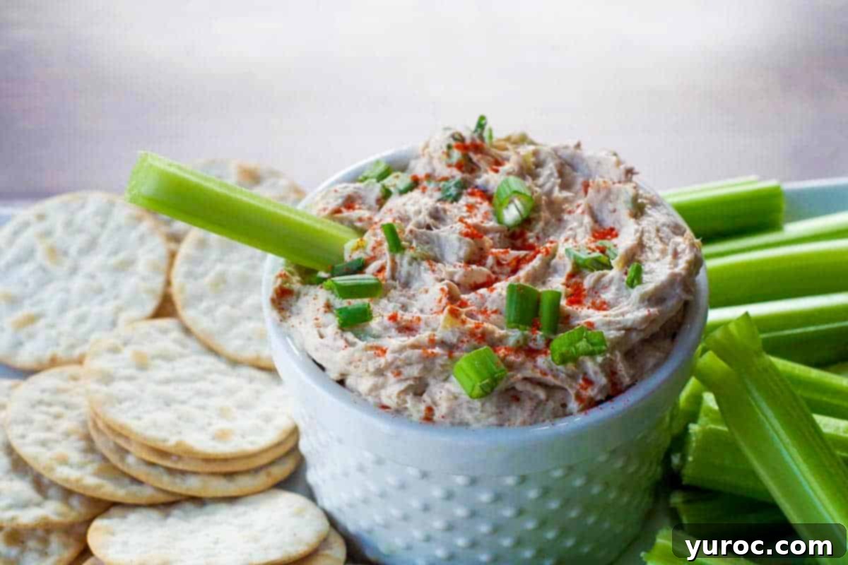 Creamy Tuna Dip 6 Finished tuna dip in a white serving container, garnished with fresh green onions and paprika, surrounded by crackers and celery sticks.