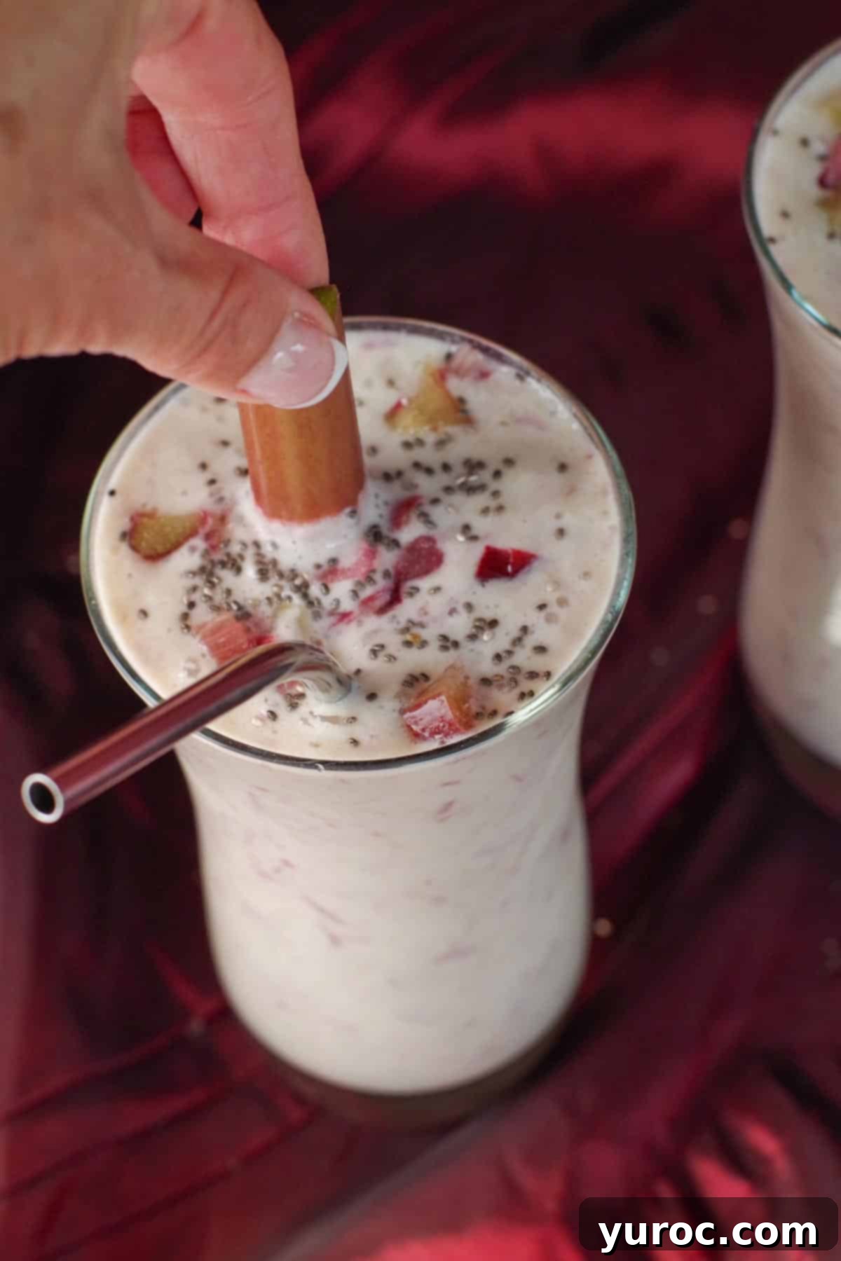 A vibrant rhubarb smoothie with a hand reaching for a piece of fresh rhubarb nestled within the drink