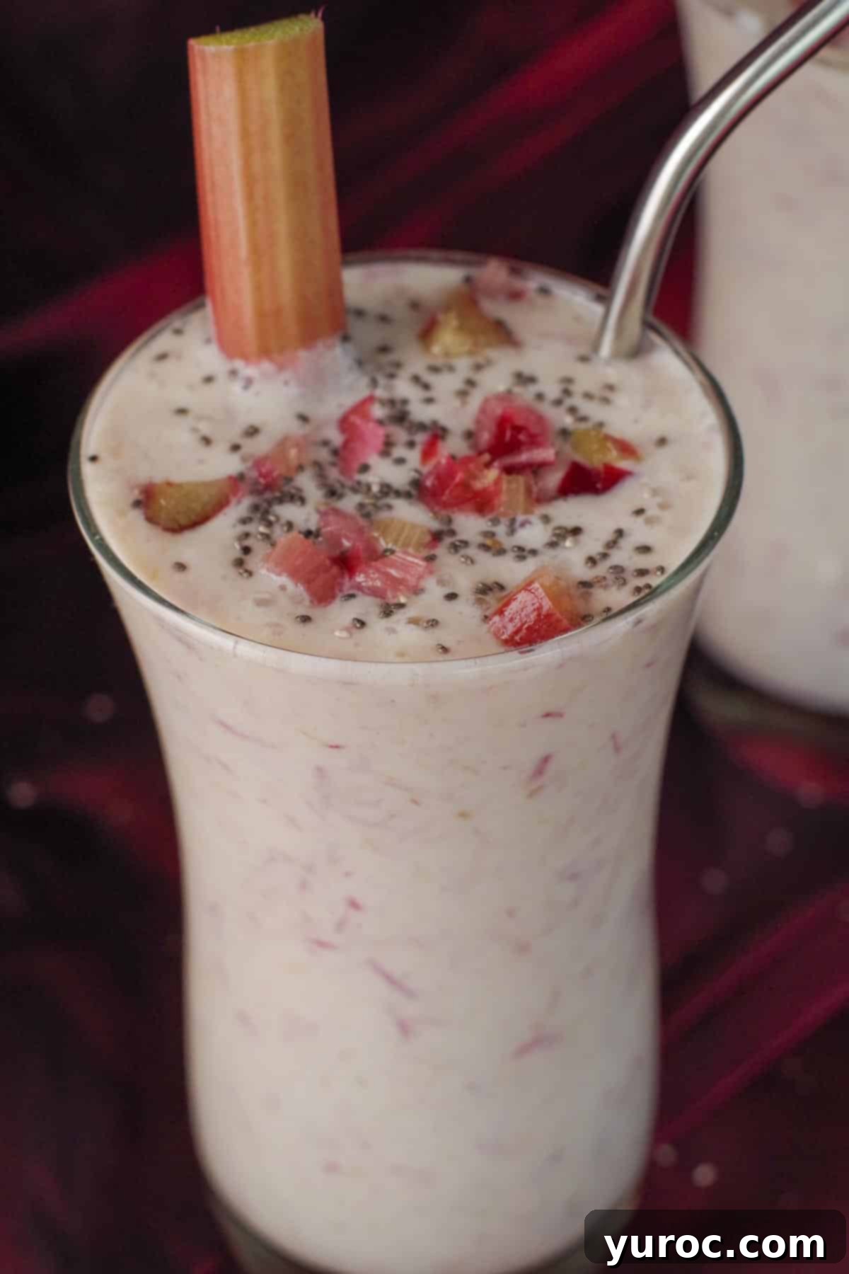 A single tall glass of healthy rhubarb smoothie, garnished with a piece of rhubarb