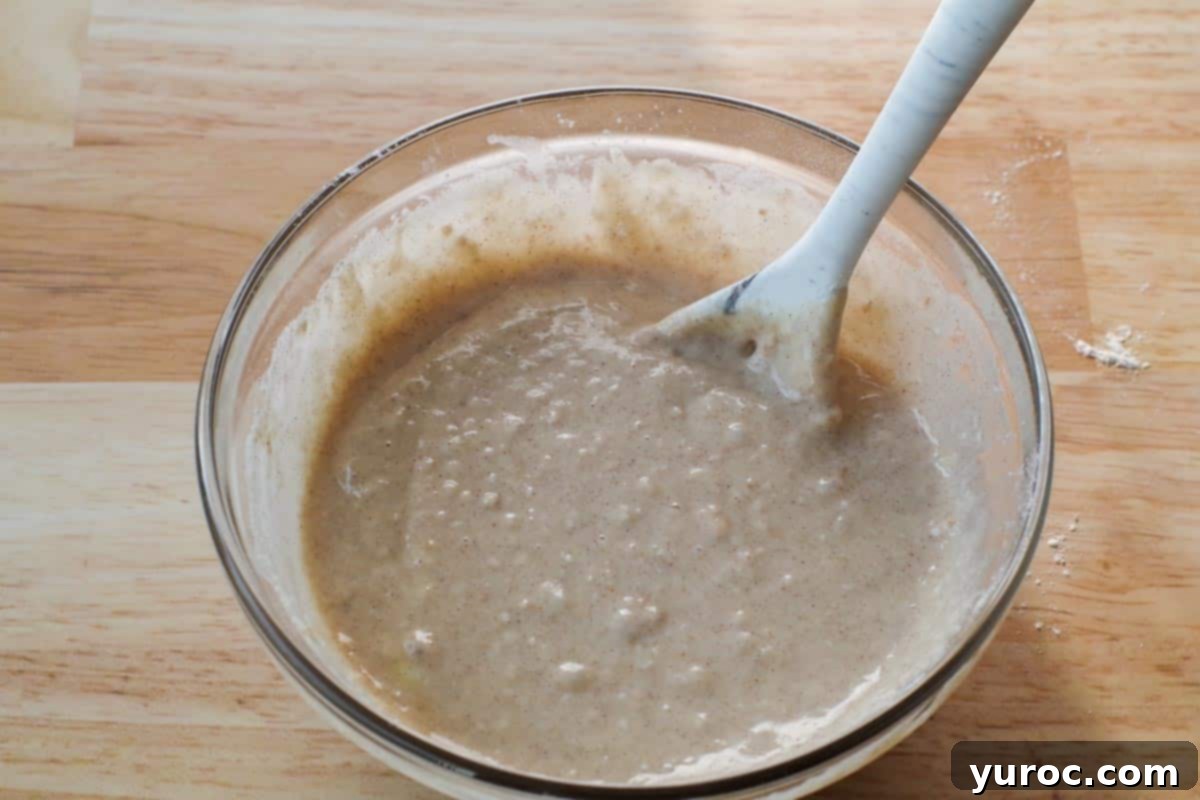 Wet and dry ingredients are quickly stirred together in a glass bowl, forming a lumpy pancake batter.