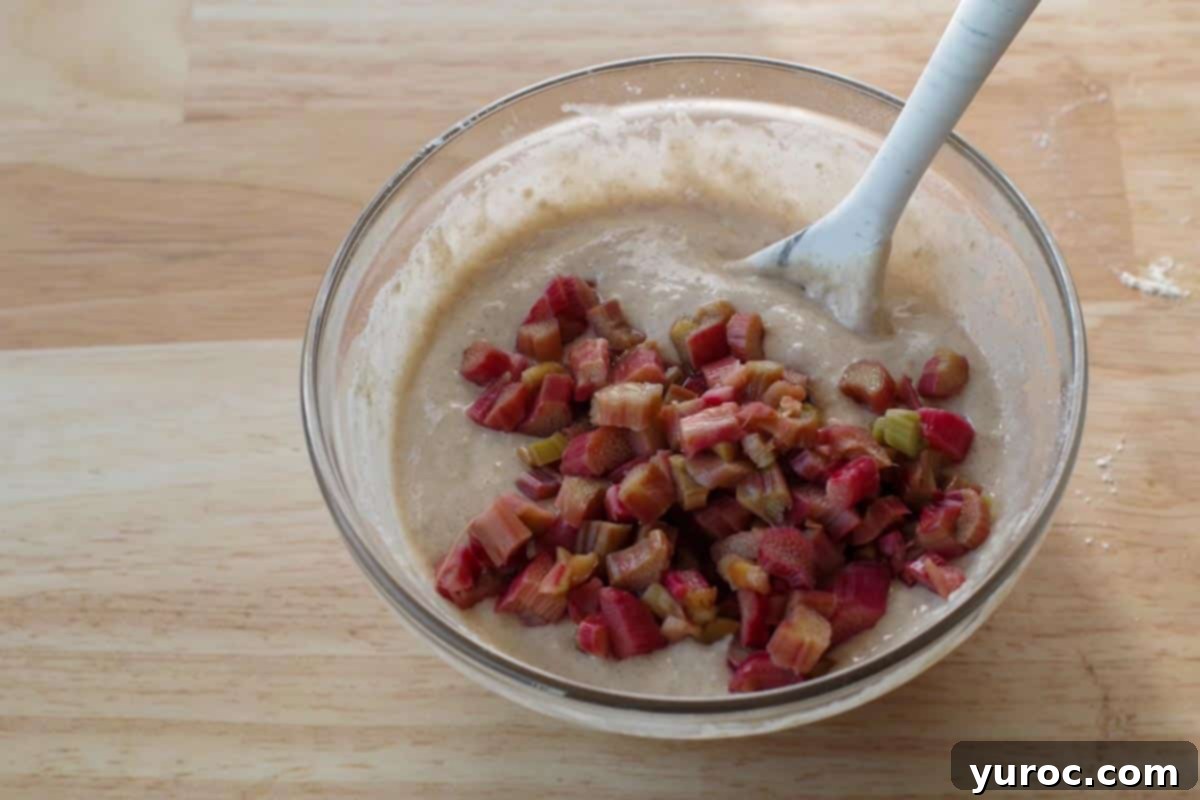 Cooked rhubarb pieces are added to the lumpy pancake batter in a glass bowl.