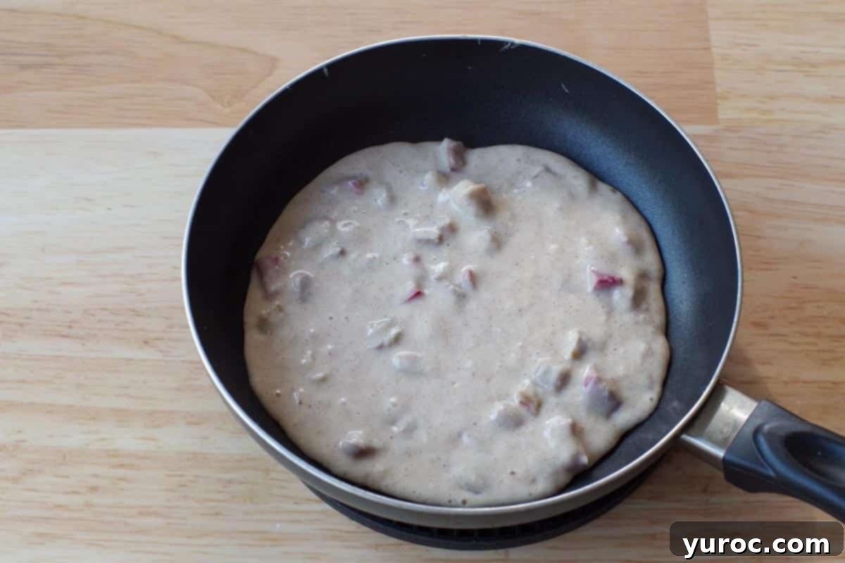 A scoop of rhubarb pancake batter cooking on a hot frying pan.