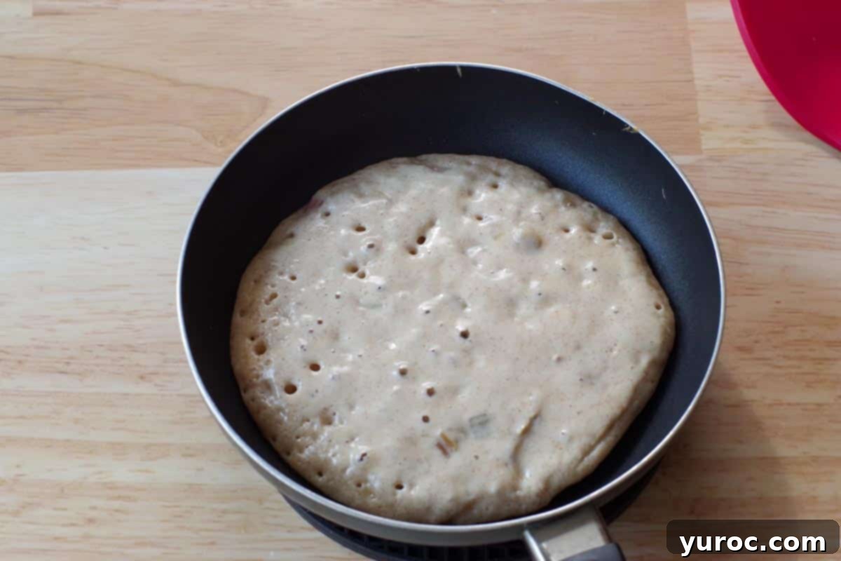 A pancake cooking in a frying pan, showing bubbles forming on its surface, indicating it's ready to be flipped.