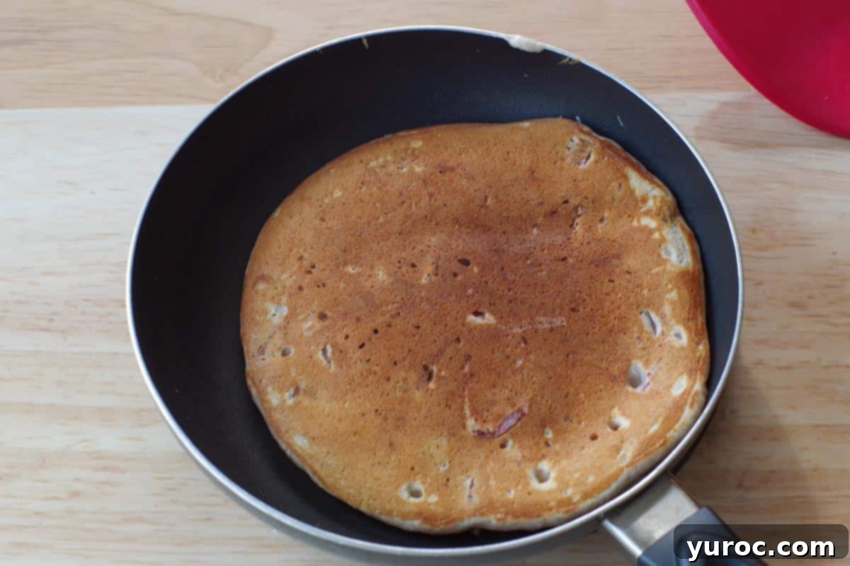 Pancakes have been flipped in the frying pan and are cooking on the second side to a golden brown.