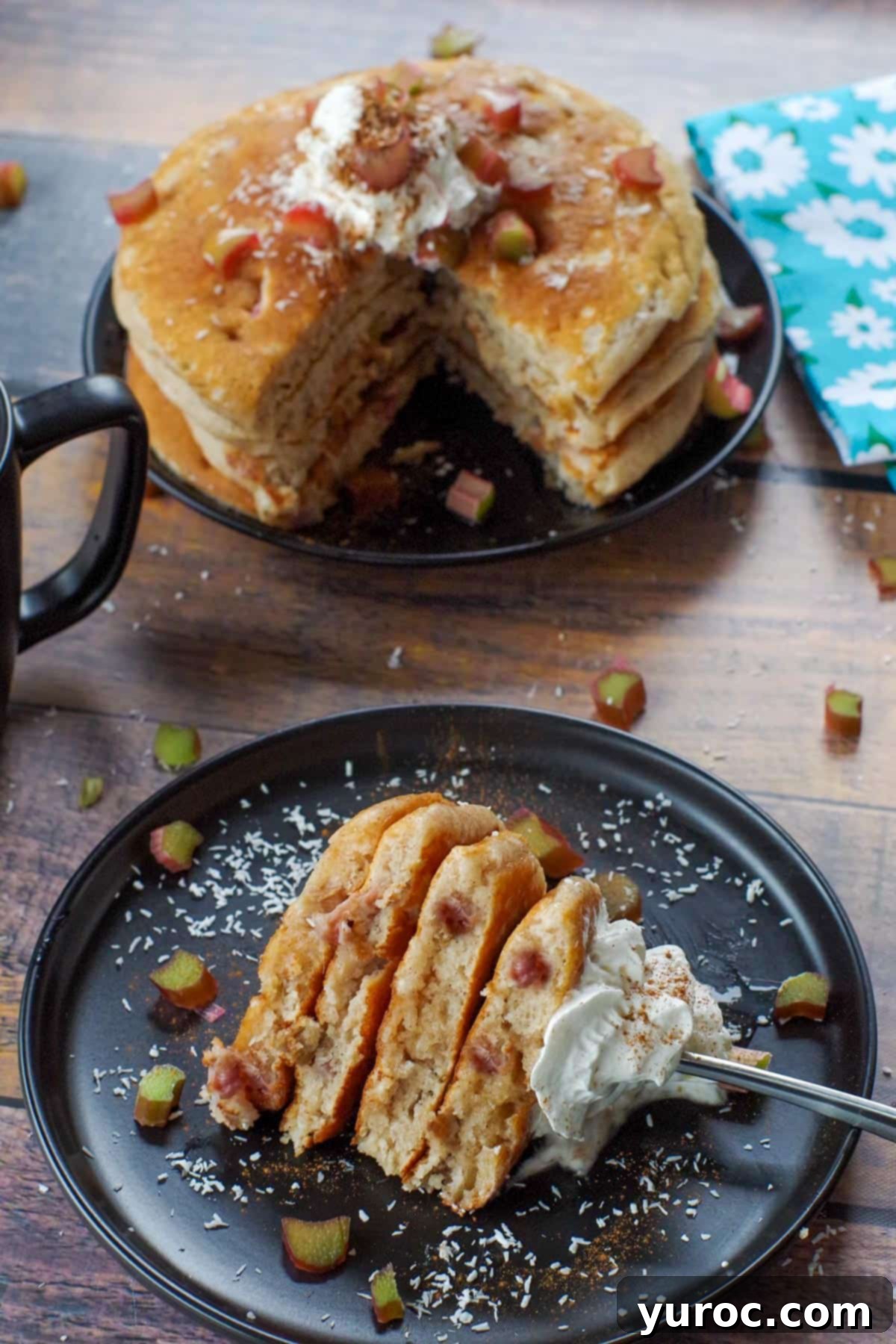 A single piece of a rhubarb pancake, cut out from a larger one, sits on a black plate with a fork, with a blurred stack of pancakes in the background.