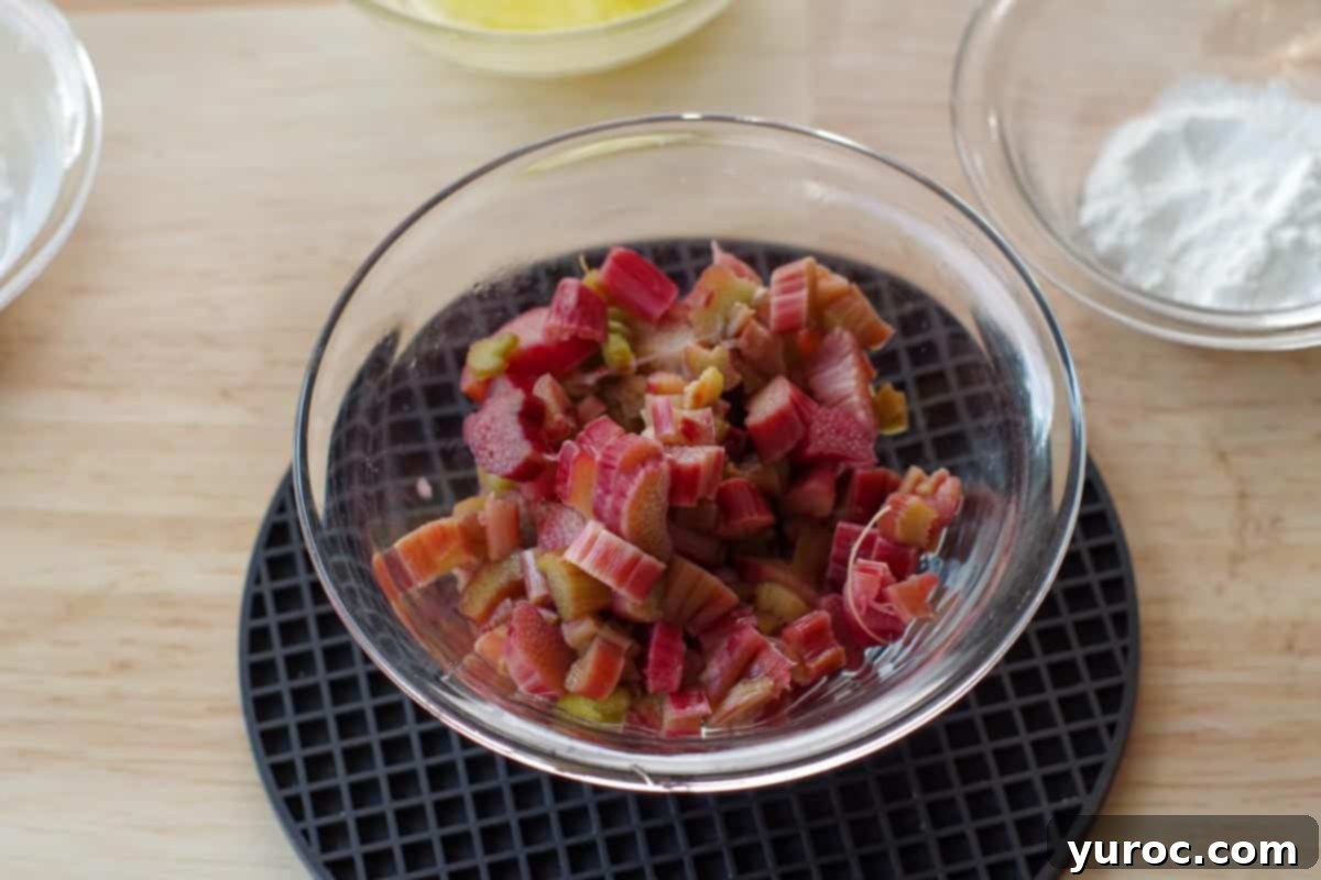 Cooked rhubarb in a clear glass bowl resting on a black trivet, showing softened pink and green pieces.