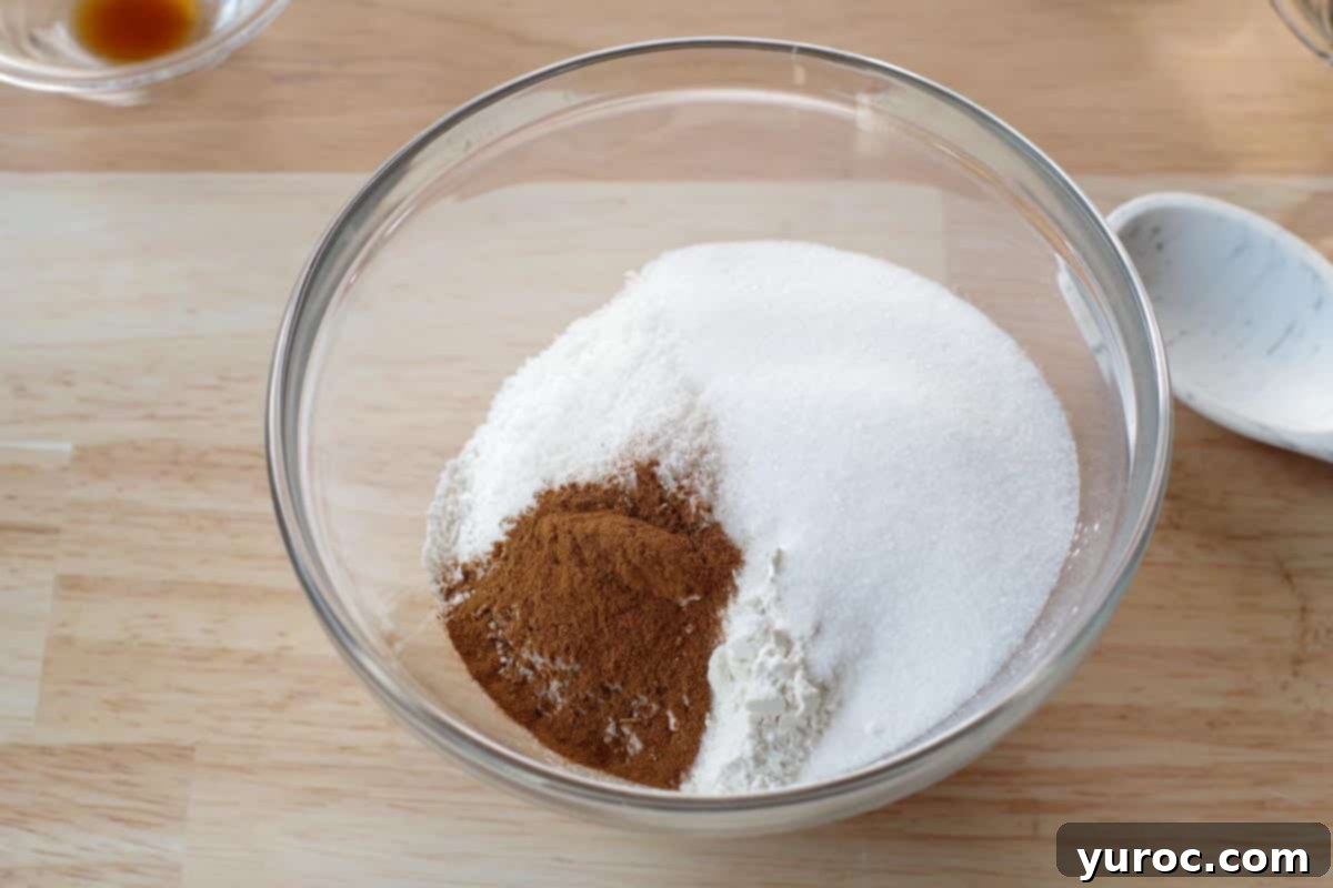Dry ingredients including flour, sugar, cinnamon, coconut flakes, baking powder, and salt are carefully added into a large glass mixing bowl.