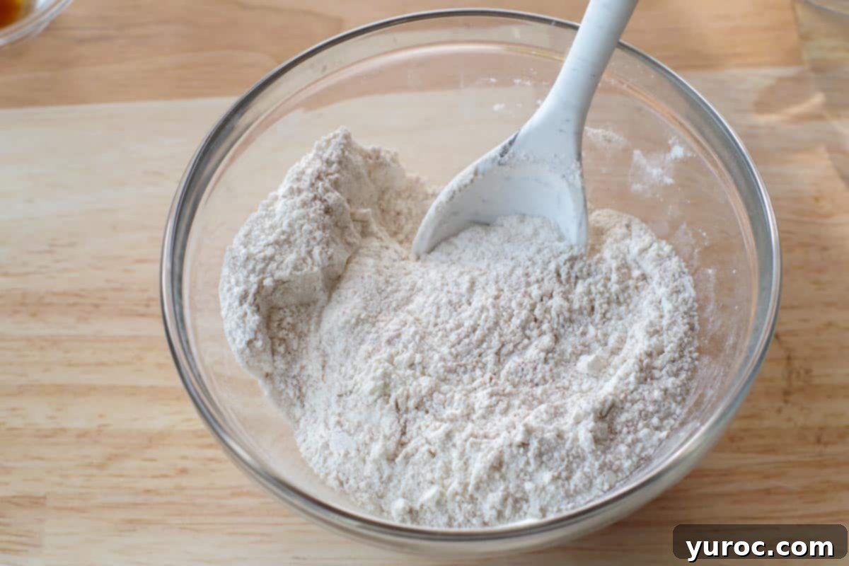 A spoon is used to thoroughly mix the dry ingredients in a glass bowl, ensuring they are evenly distributed.
