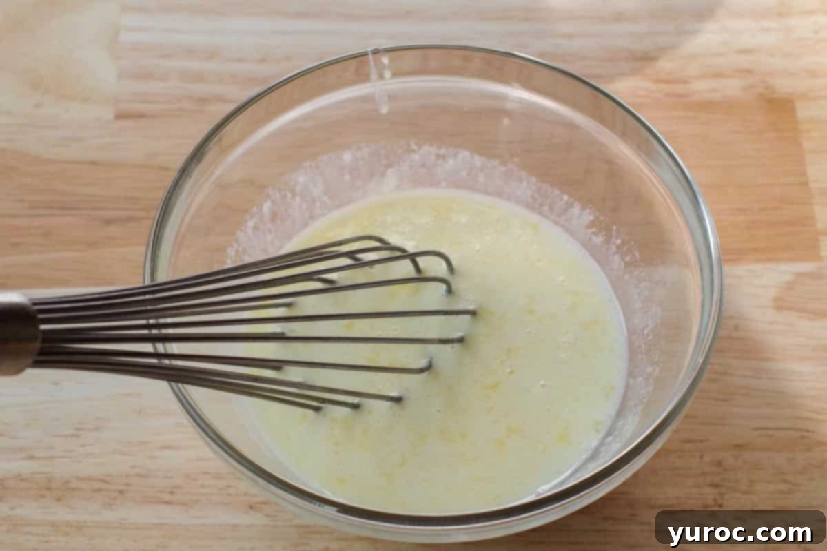Wet ingredients, including egg, milk, melted butter, and extracts, are whisked together in a separate glass bowl.