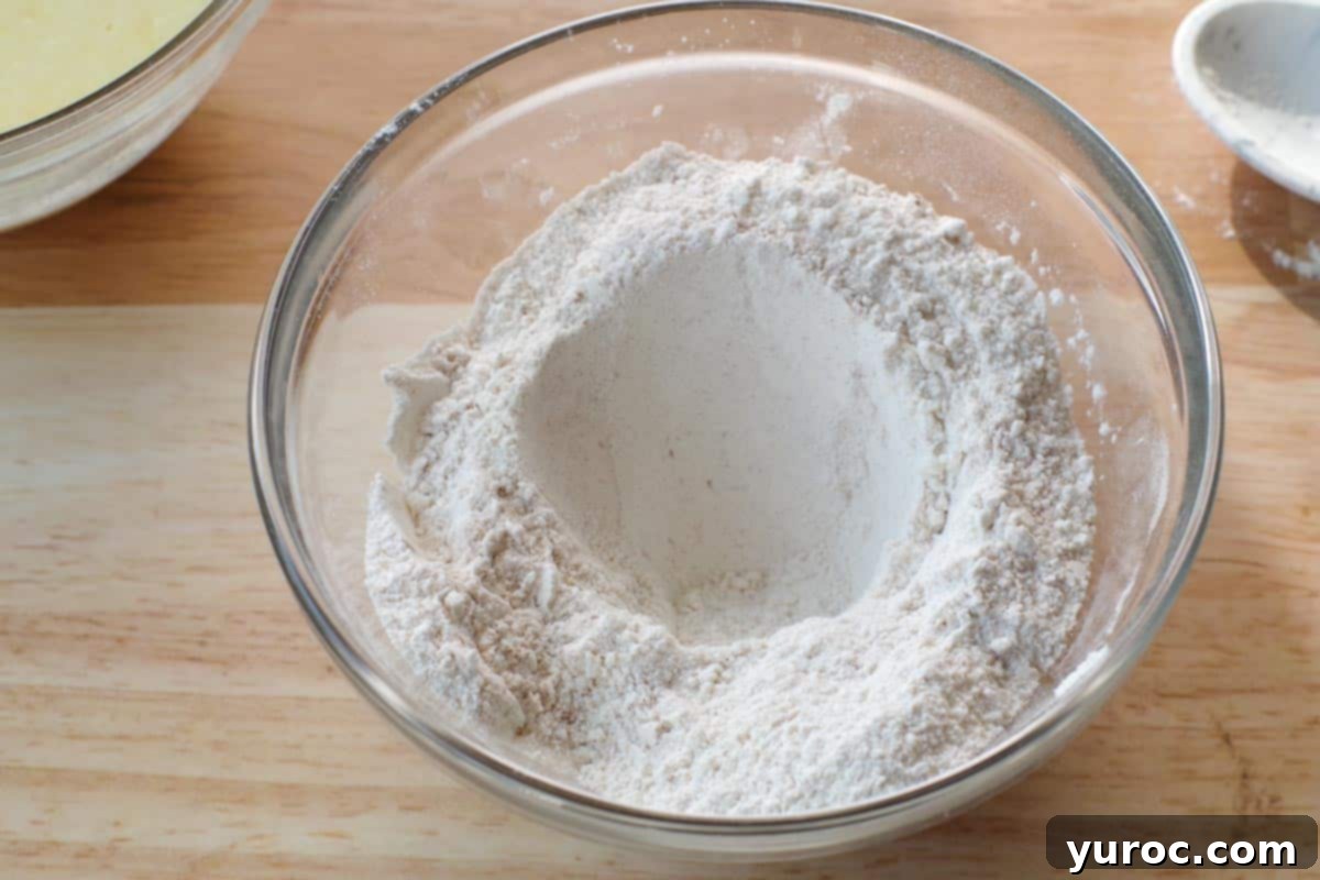 A well (hole) is formed in the center of the dry ingredients in a glass mixing bowl, ready for the wet mixture.