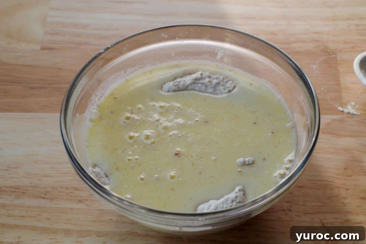 The whisked wet ingredients are gently poured into the well created in the dry ingredients in a glass mixing bowl.