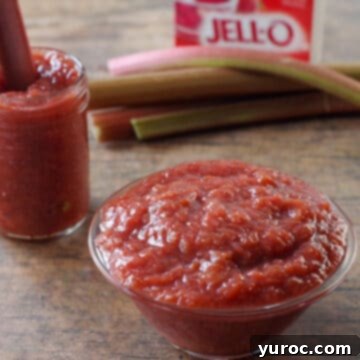 stewed rhubarb in glass bowl with jar of stewed rhubarb and fresh rhubarb and a box of strawberry jello in the background.