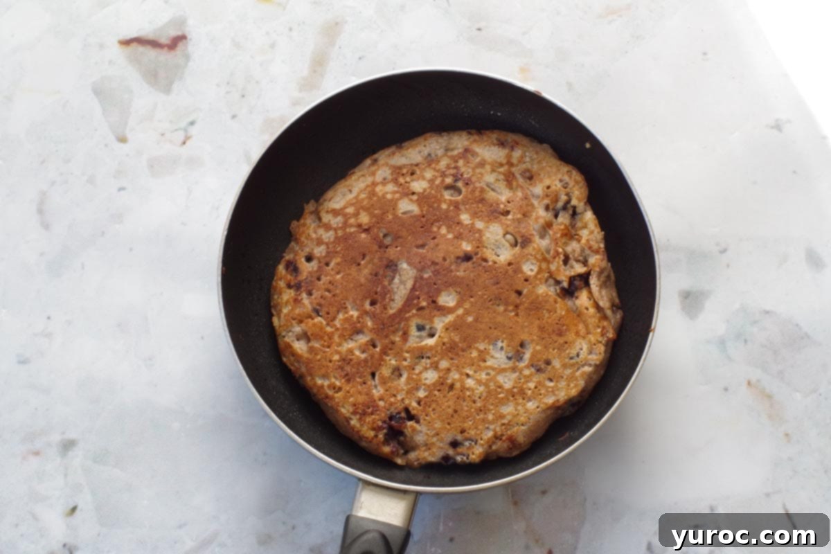A perfectly cooked Saskatoon Berry pancake, flipped over and golden brown, ready to be removed from the pan.