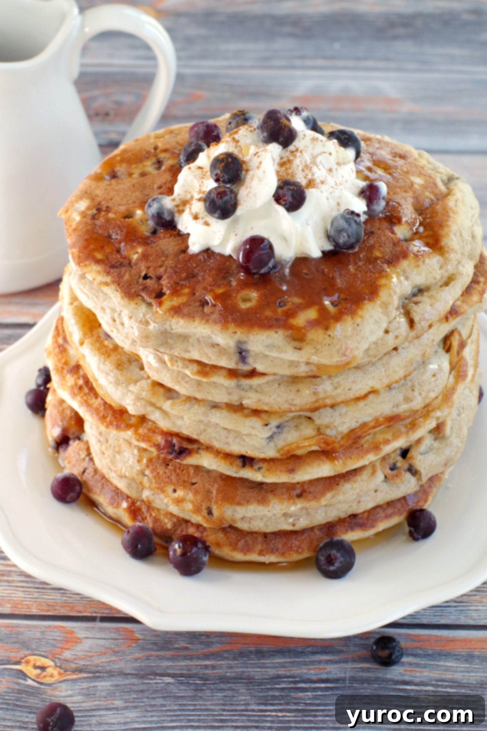 A beautifully arranged stack of Saskatoon Berry Pancakes, generously topped with whipped cream and an abundance of fresh Saskatoon berries, making for an inviting breakfast.