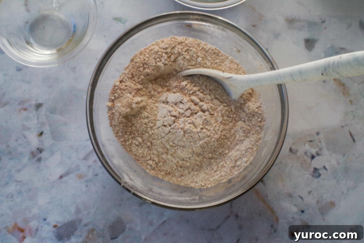 A large silicone spoon mixing dry ingredients in a glass bowl, ensuring they are well combined.