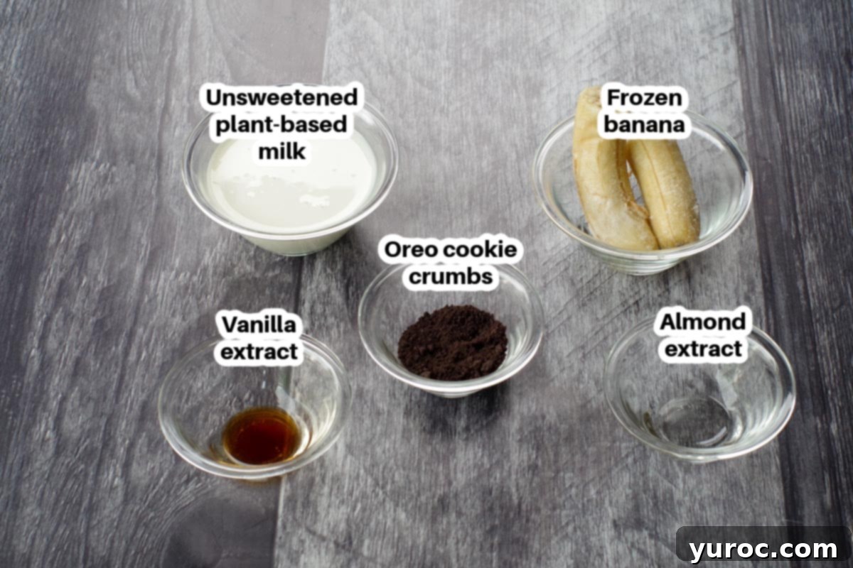 Guilt-Free Oreo Banana Milkshake 3 Individual glass bowls containing each ingredient for the Oreo banana milkshake, clearly labelled: frozen banana, Oreo baking crumbs, plant-based milk, almond extract, and vanilla extract.