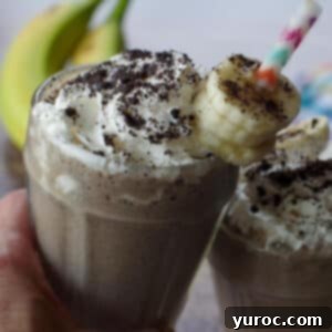 Guilt-Free Oreo Banana Milkshake 9 Two glasses of Healthy Oreo Banana Milkshake clinking together, with fresh bananas in the soft-focus background.