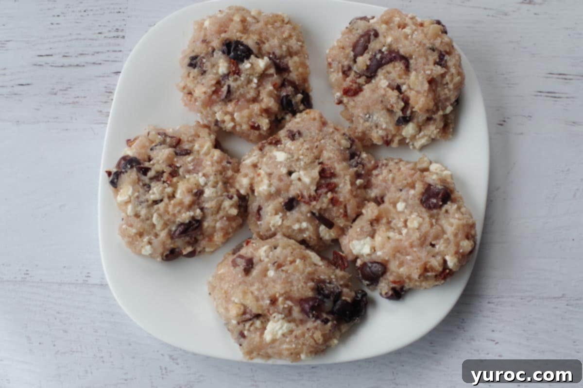 6 Greek chicken burger patties on a white plate, ready to be cooked