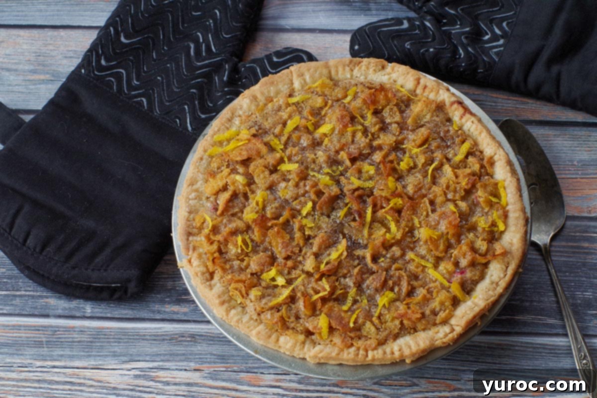 A freshly baked Rhubarb Sour Cream Pie, golden brown and glistening, cooling on a wire rack with orange zest as a garnish.