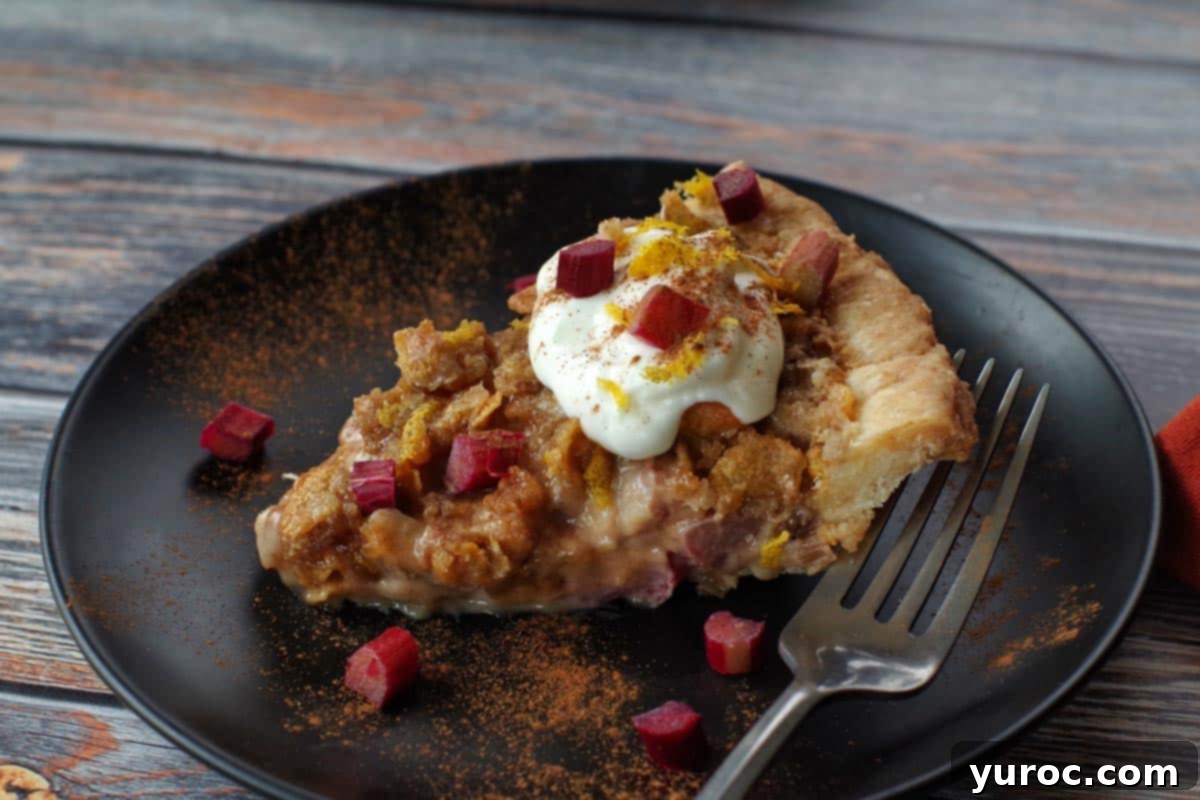 A close-up shot of a single slice of Rhubarb Sour Cream Pie on a black plate, showcasing the creamy filling, visible rhubarb pieces, and the irresistible crunchy cornflake topping.