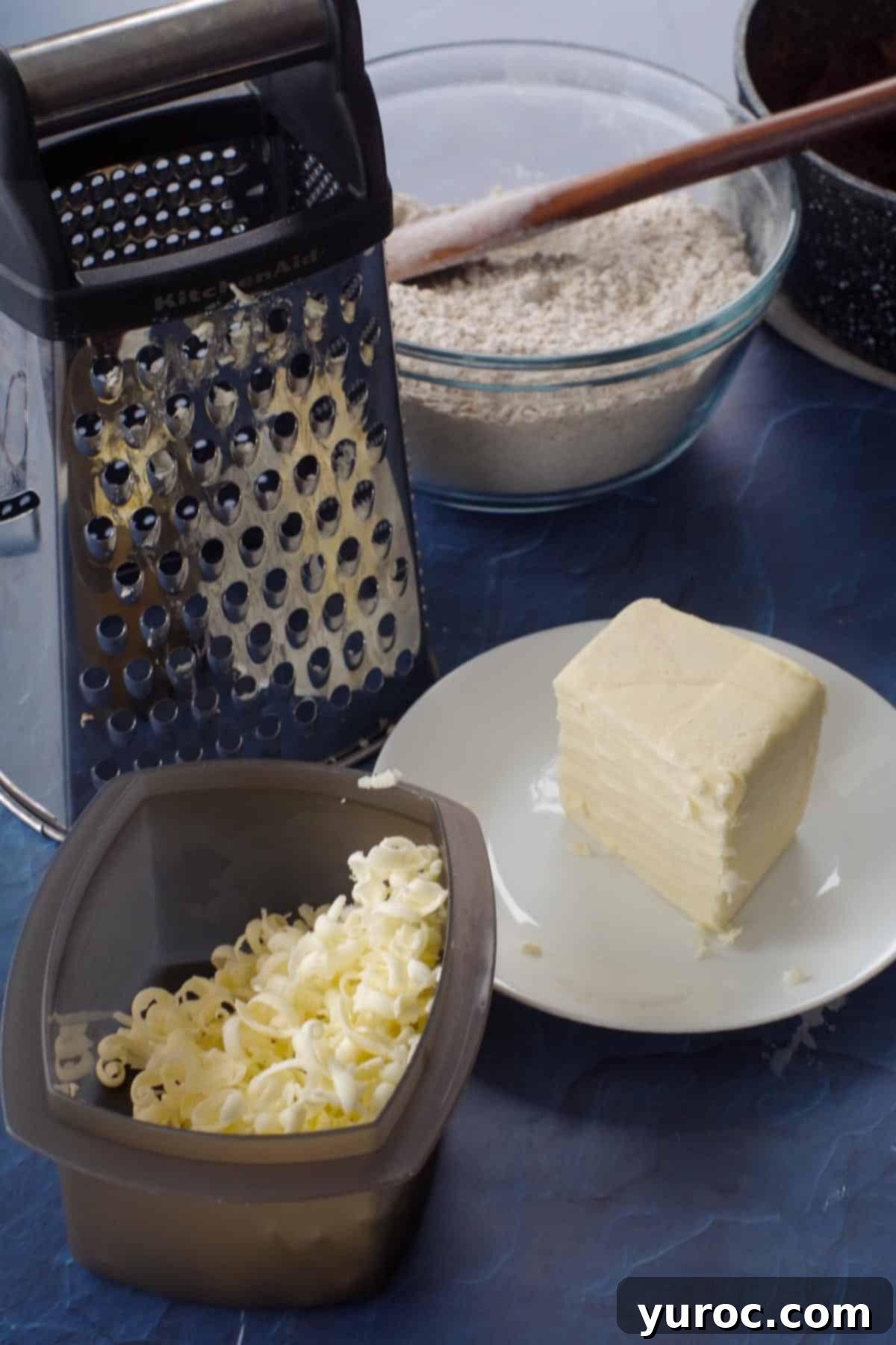 A block of frozen butter being grated over a bowl of dry ingredients for a crumb topping, illustrating an expert tip.