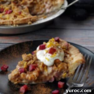 A slice of creamy Rhubarb Sour Cream Pie with a crunchy topping, placed on a black plate with a fork, and the full pie in the background.