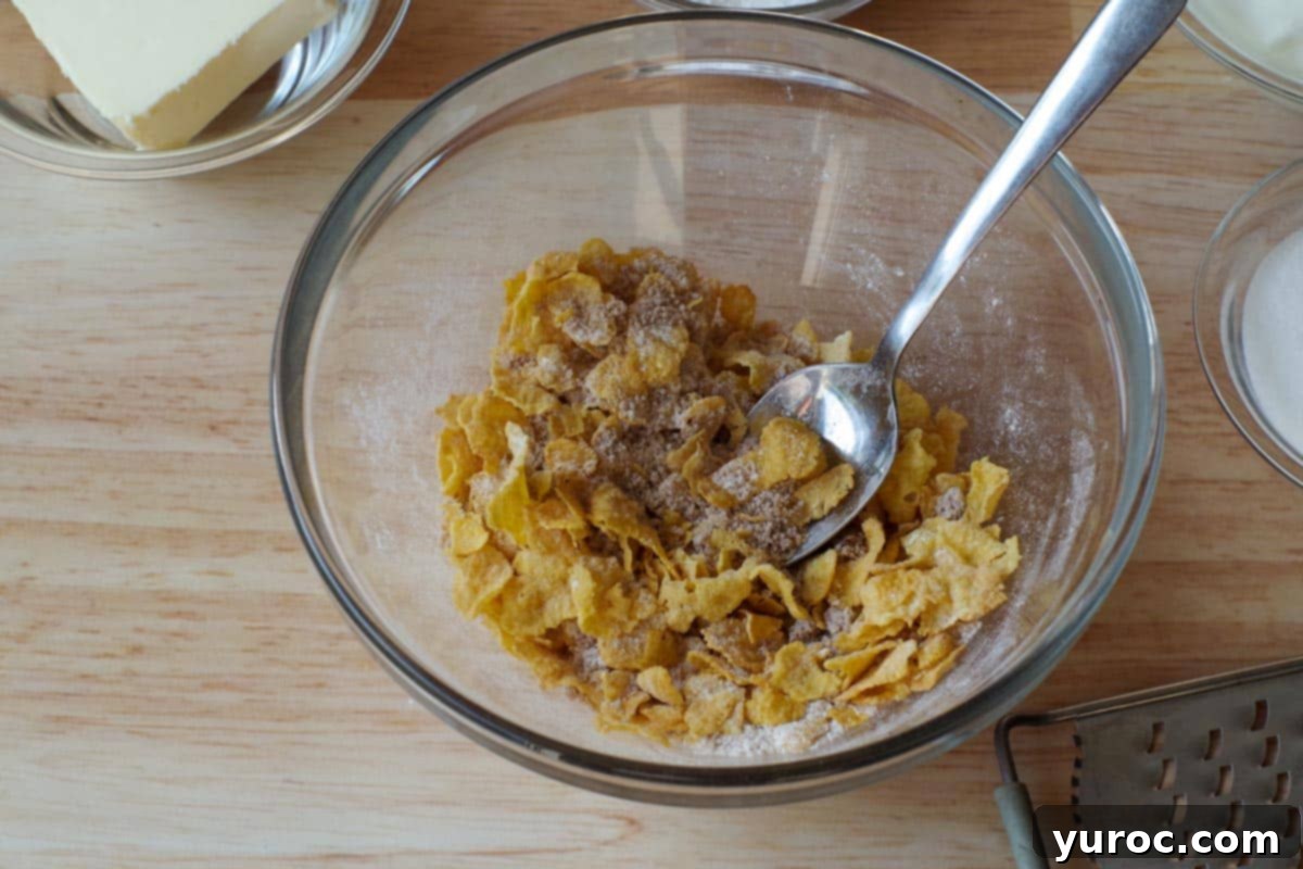 Crushed cornflakes, brown sugar, and flour being mixed together in a glass bowl to create the crunchy pie topping.