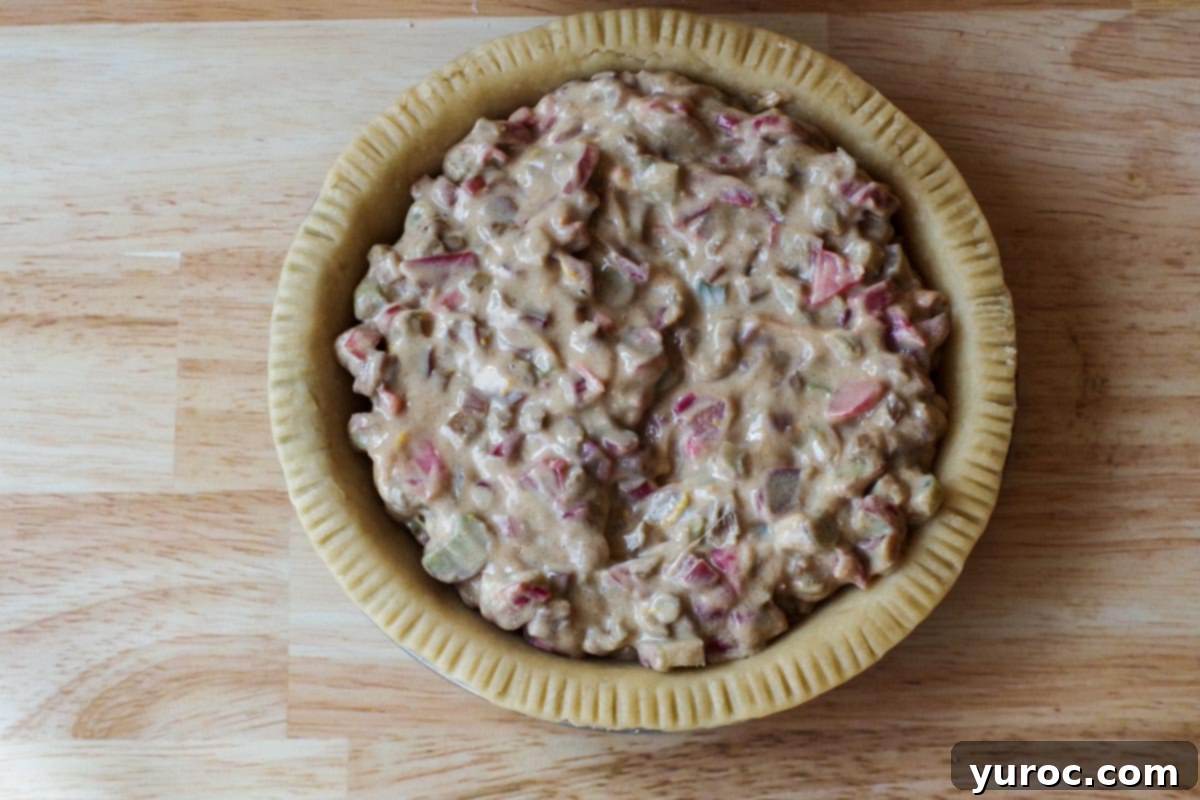 The rhubarb sour cream pie filling being carefully poured into an unbaked pie crust.