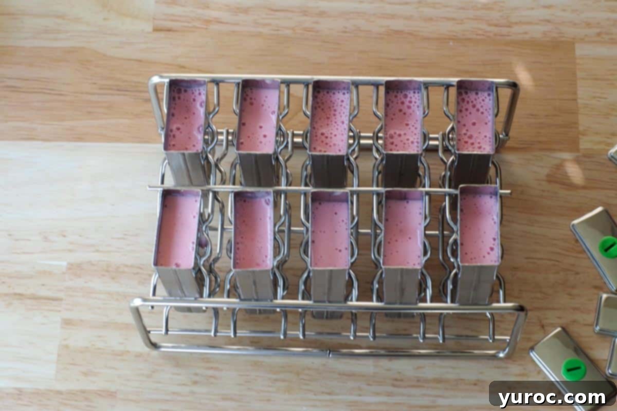Ten popsicle molds are filled with the strawberry yogurt mixture, ready for the next step.