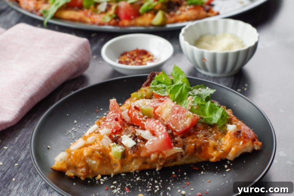 close up of piece of big mac pizza on a black plate with whole pizza in the background