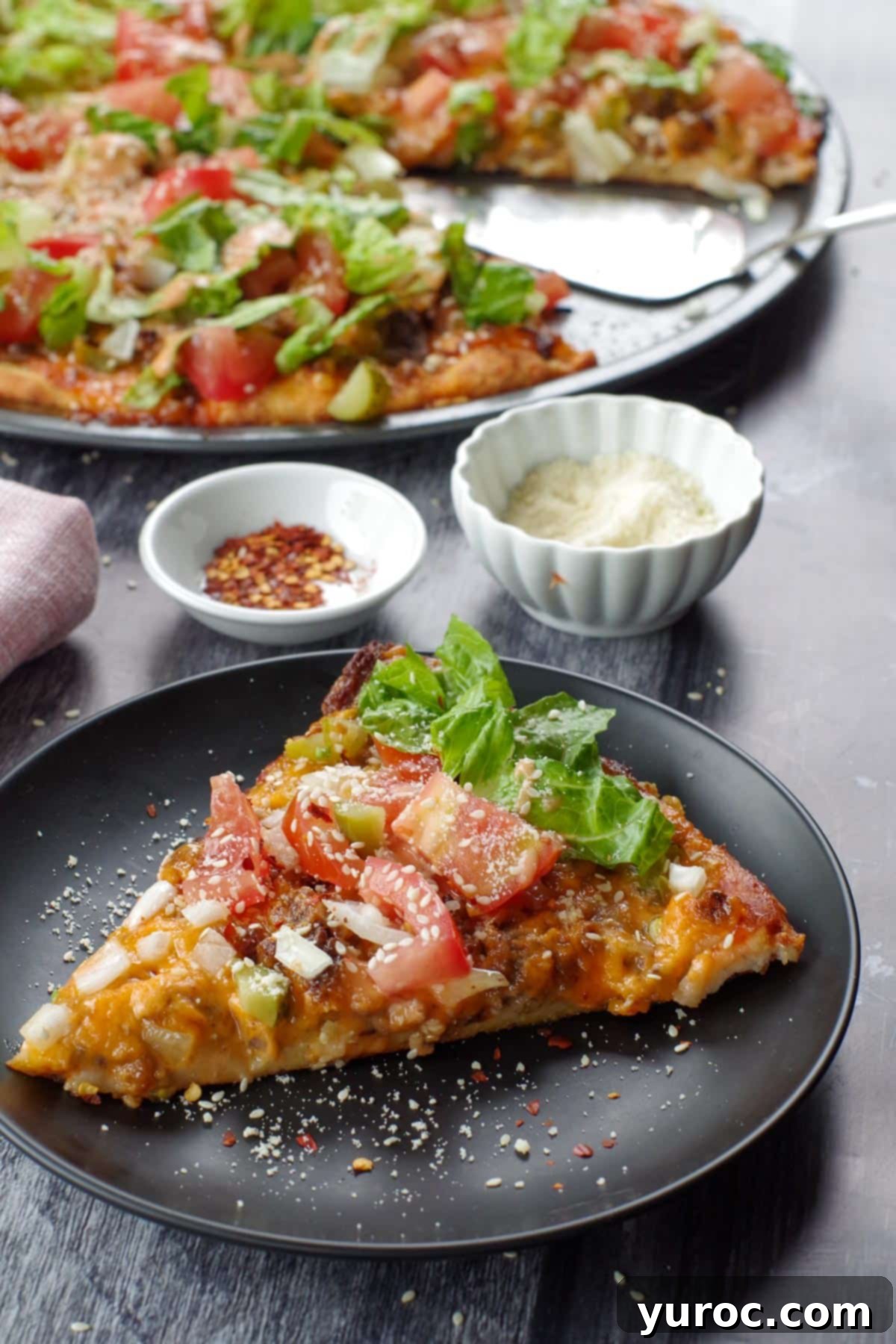 piece of big mac pizza on a black plate with whole pizza in background