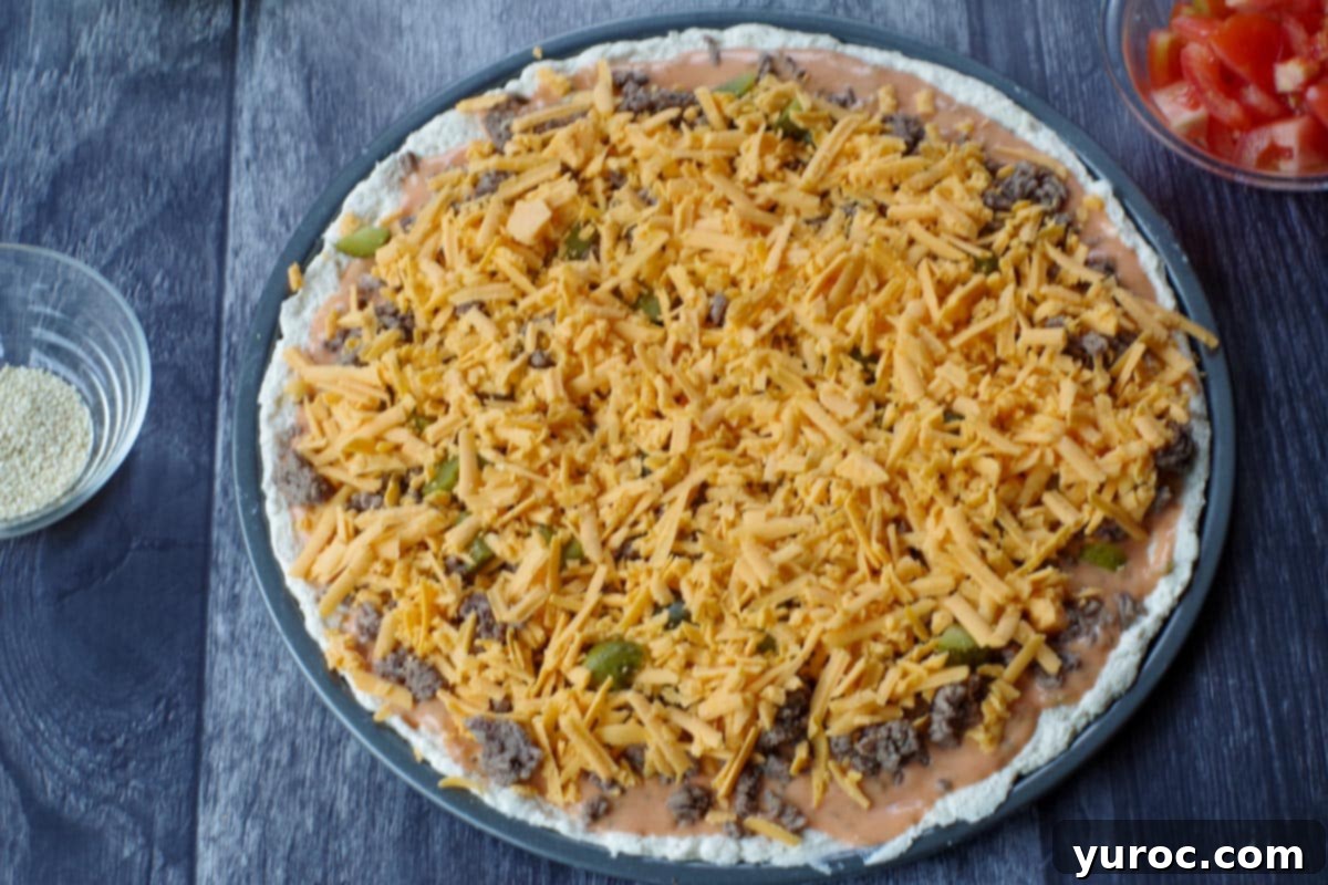 uncooked big mac pizza with shredded cheese added on top of sauce, ground beef and pickles