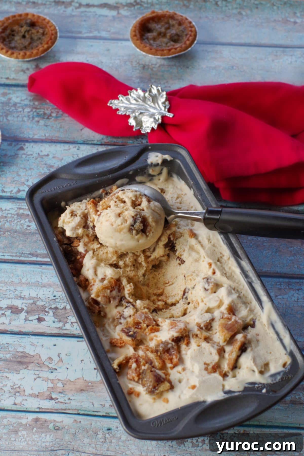 Effortless Butter Tart Dream Ice Cream 1 Scooping rich butter tart ice cream from a loaf pan, with a red maple leaf napkin and whole butter tarts in the background, showcasing its creamy texture and visible tart pieces.