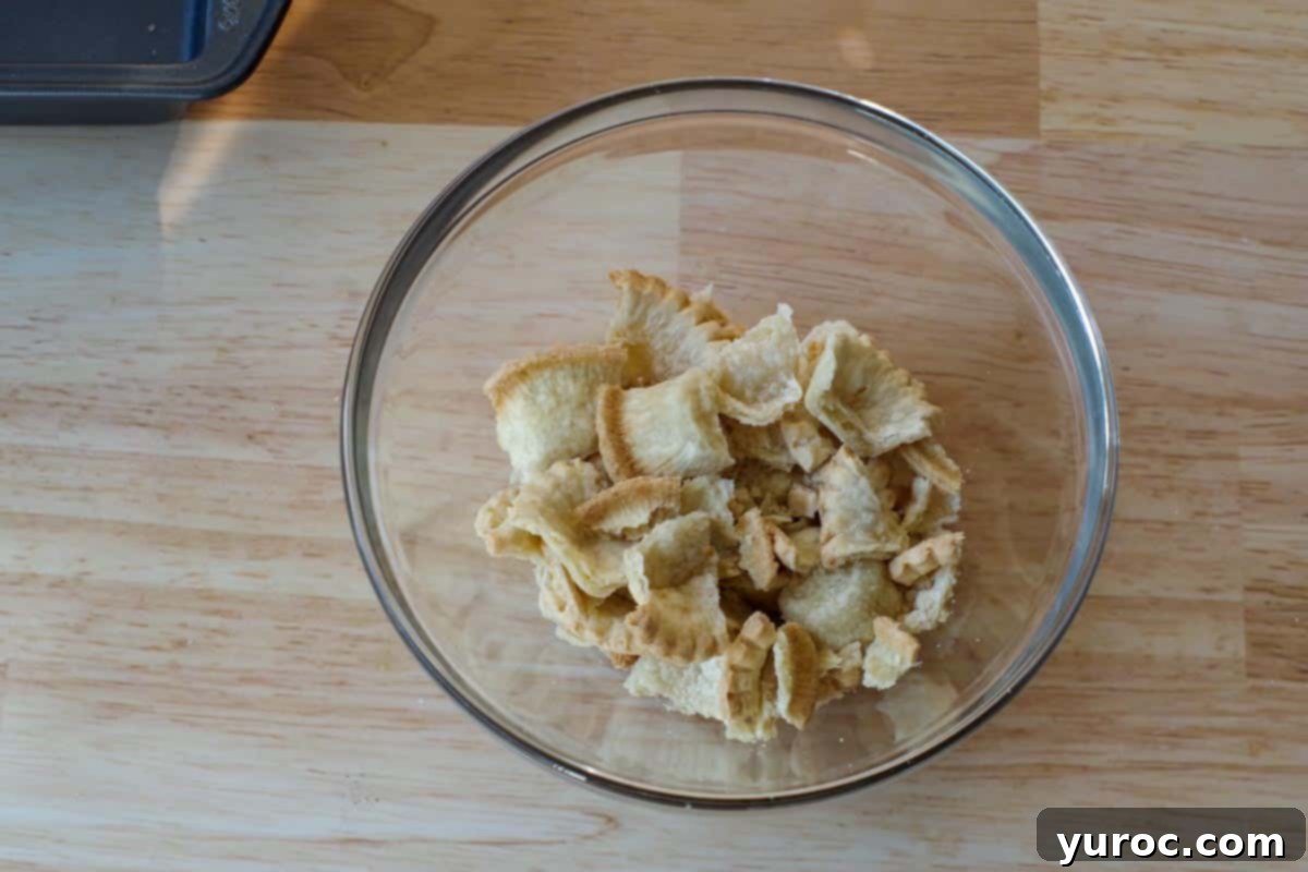 Effortless Butter Tart Dream Ice Cream 11 Baked mini tart shells broken into small, uneven pieces in a medium glass bowl.