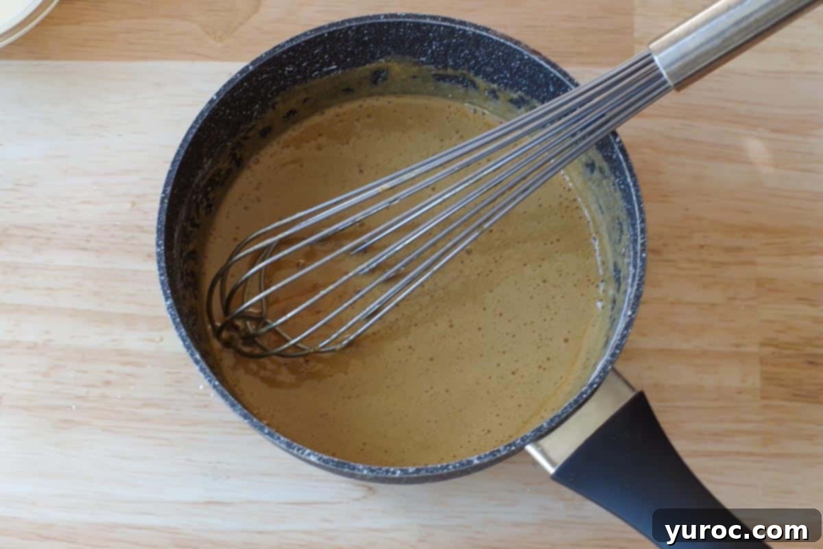 Effortless Butter Tart Dream Ice Cream 6 Thickened butter tart sauce, resembling gravy, in a saucepan with a whisk, showing its smooth, rich consistency.