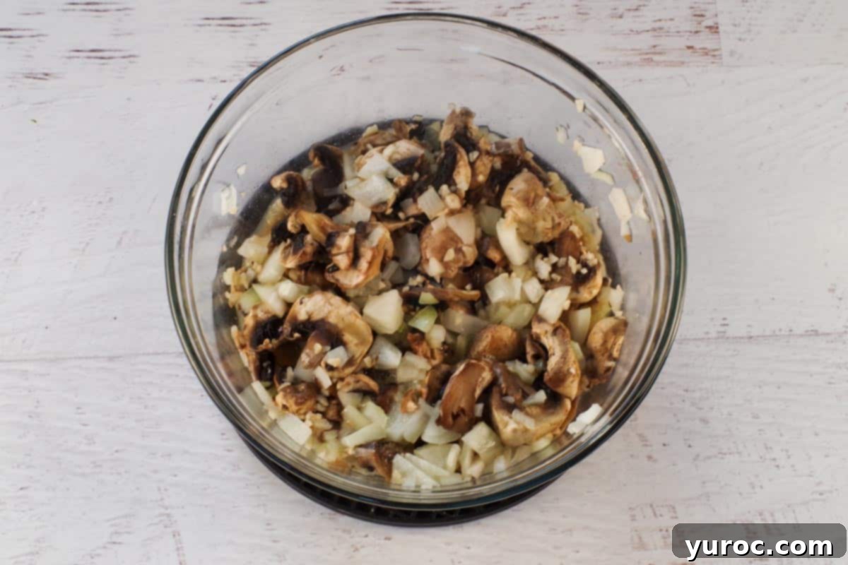 Cooked mushrooms and onions, softened and fragrant, in the same glass bowl after microwaving.