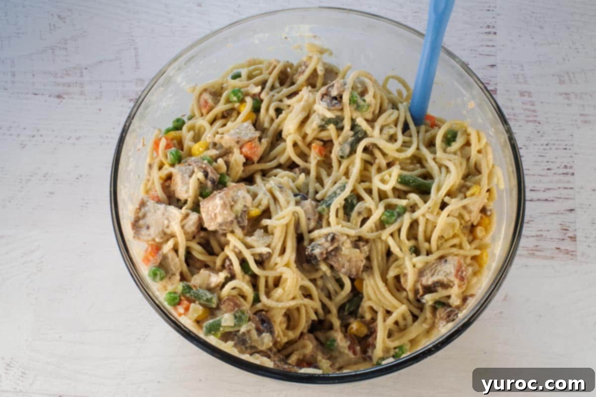 A large mixing bowl containing cooked spaghetti, turkey, mushroom-onion mixture, and other sauce ingredients, thoroughly combined before adding cheese.