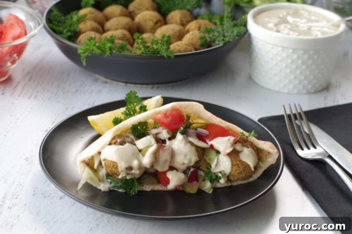 Crispy Air Fryer Falafel from Mix 11 air fryer falafel pita on a black plate with a bowl of falafel balls in the background